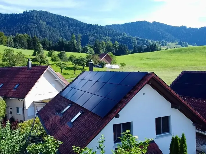 Einfamilienhaus mit schwarzer Photovoltaikanlage vor Wiesen und Wald